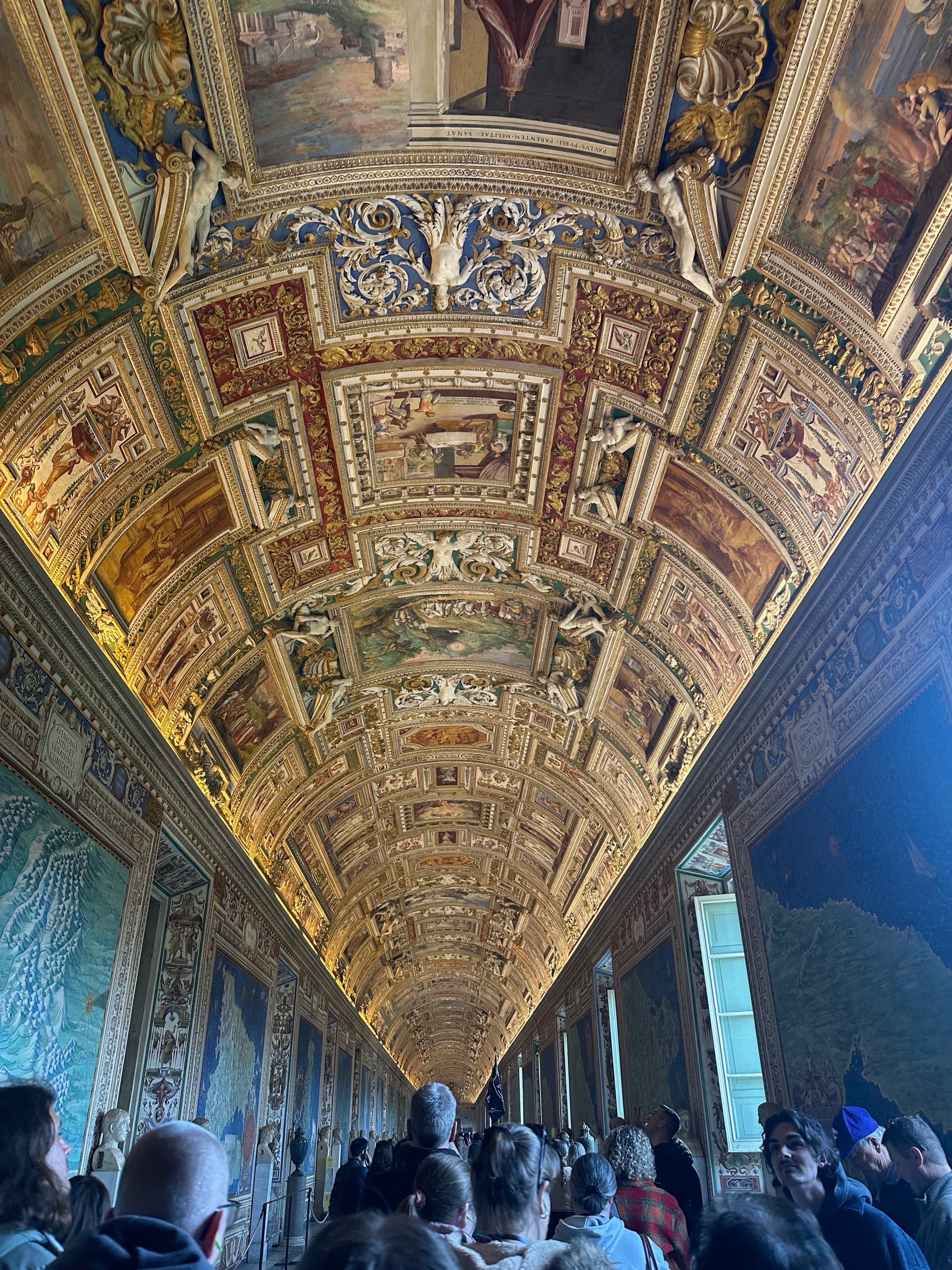 Crowd walking beneath ornate ceilings in the Vatican Museums
