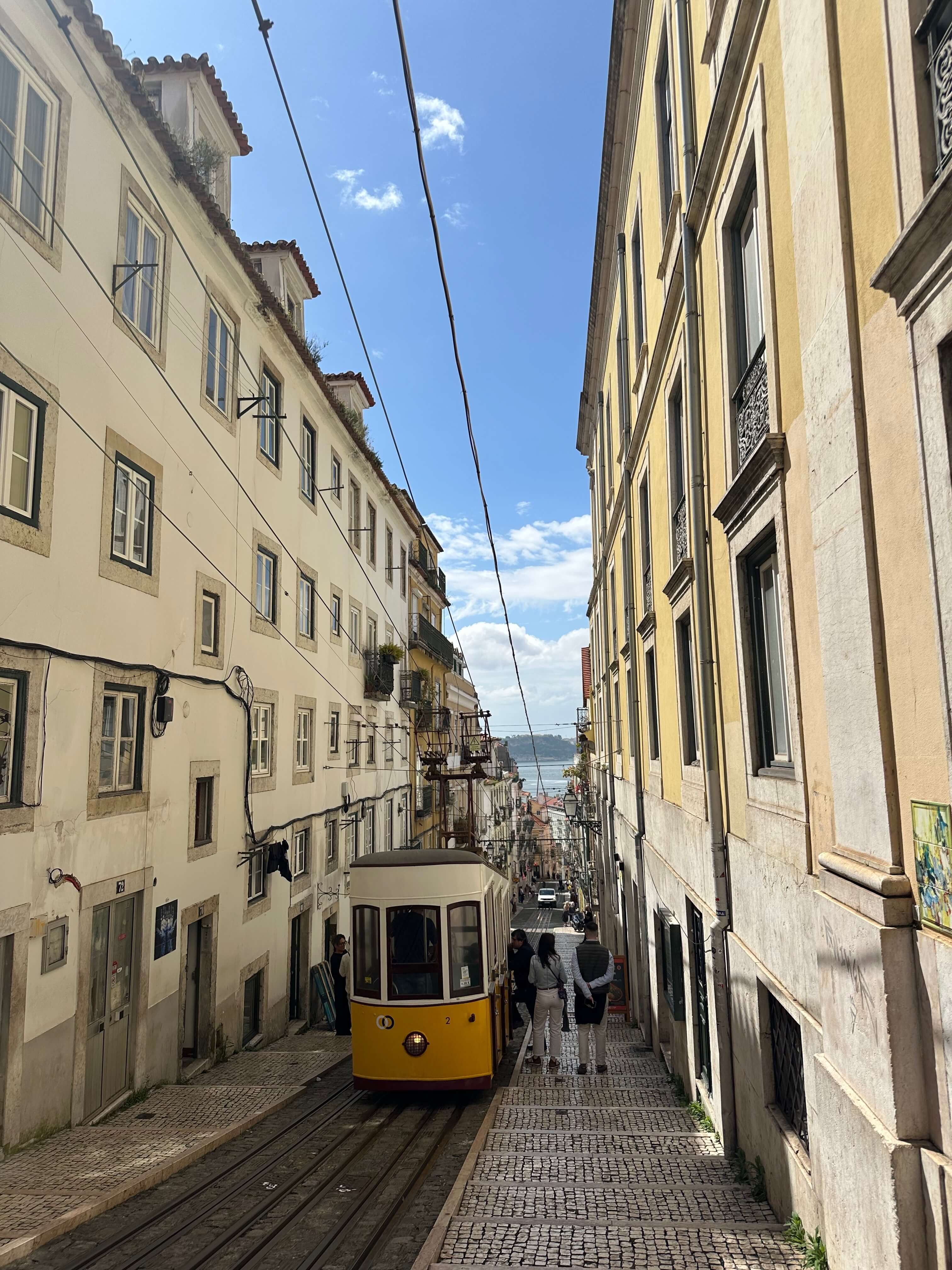 Yellow tram descending a Lisbon hill toward the Tagus River